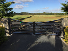 Load image into Gallery viewer, Wooden gate at the end of a driveway leading to a rural landscape with fields and trees.